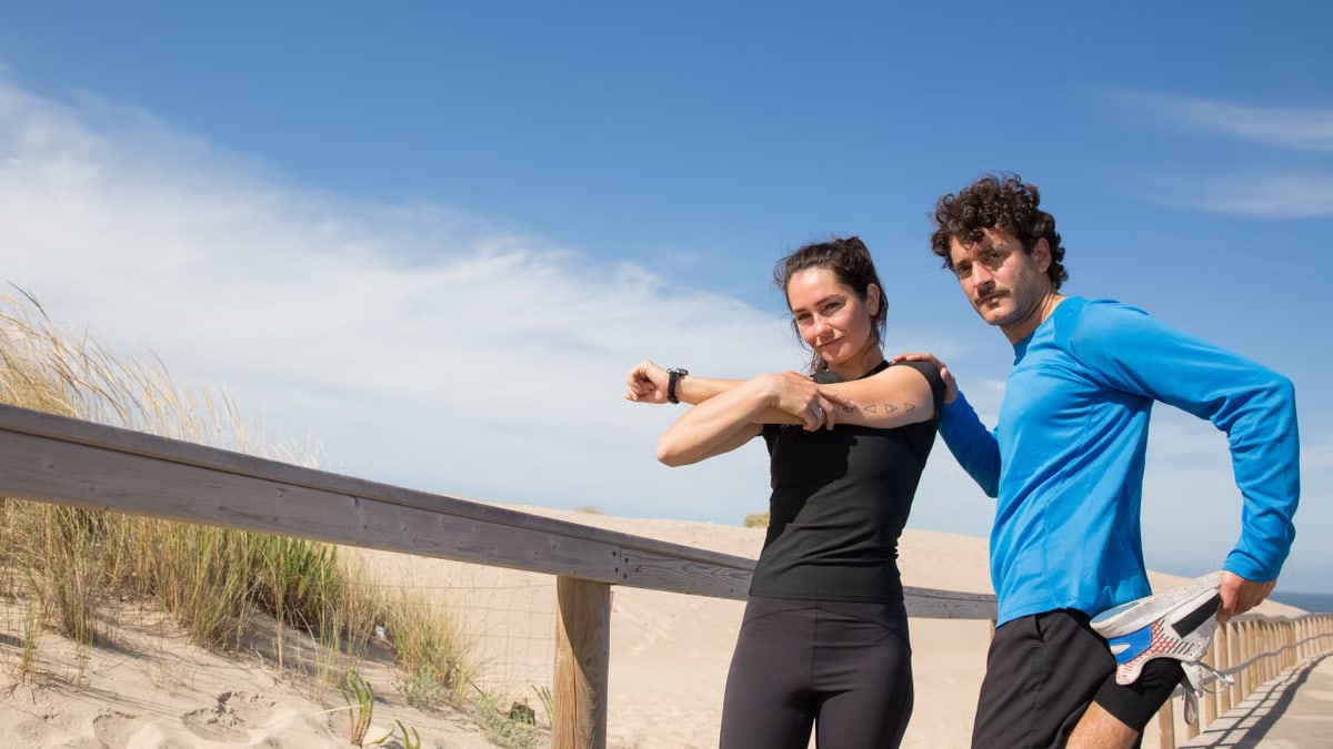 A man and woman in activewear stretch on a sunny Portugal beach boardwalk, promoting fitness and outdoor activities.